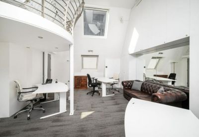 Spacious open-plan office with white desks and a brown leather Chesterfield sofa.