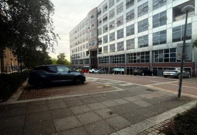 Modern multi-story office building with large glass windows and a paved parking area.