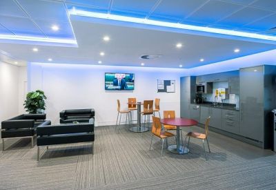 Modern communal kitchen and breakout area with blue neon accent lighting and colorful tables.