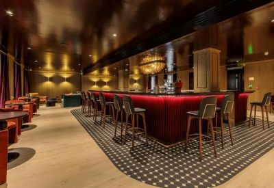 Dimly lit bar and lounge with a curved red velvet counter and plush seating.
