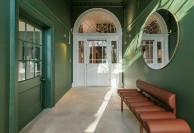 Bright hallway with green walls, a leather bench, and a large circular mirror.