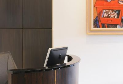 Close-up of a dark wood reception desk with a computer monitor and colorful artwork.