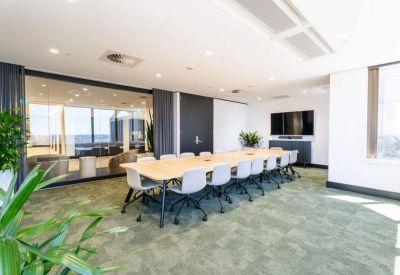 Spacious boardroom with a long wooden table, grey chairs, and a glass wall overlooking a lounge area.