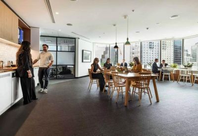 Social kitchen and dining area with wooden tables, people working, and floor-to-ceiling windows with city views.