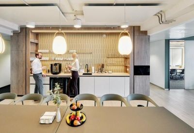 Modern office kitchen and coffee station with wooden cabinetry and bar seating.