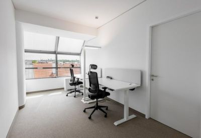 Bright two-person private office with height-adjustable desks and city views through large windows.