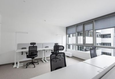 Modern open-plan office space with multiple white workstations and ergonomic black mesh chairs.