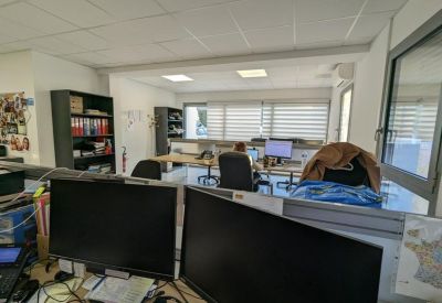 Open-plan office with multiple computer monitors and shelves in a bright room.