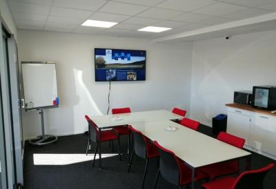 Meeting room with a white conference table, red chairs, and a wall-mounted screen.