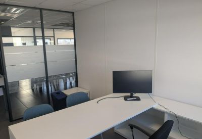 Private office featuring a white corner desk and glass partition walls.