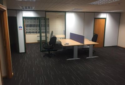 Open-plan workspace featuring a light wood desk with a purple divider and dark grey carpeting.