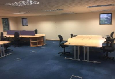 Spacious open office area with blue carpet tiles and several grouped workstations.