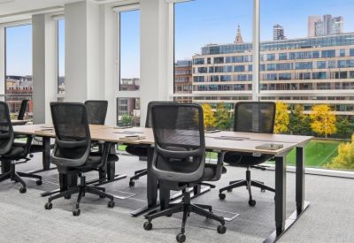 Bright office workspace with wooden desks, ergonomic chairs, and large windows.