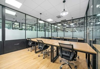 Open-plan workspace with wooden desks, black mesh chairs, and glass partition walls.