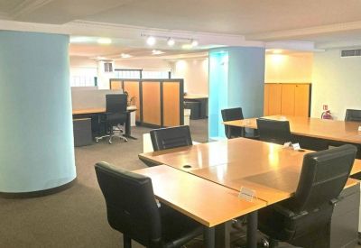 Open-plan coworking space with large wooden desks and distinctive blue architectural columns.