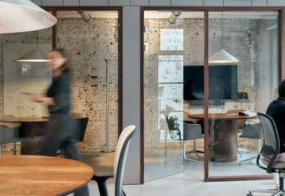 Glass-enclosed meeting room with brick walls and a blurred person walking by.