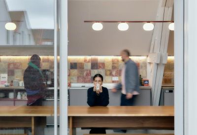 Cozy lounge area with a person drinking coffee and others walking by.
