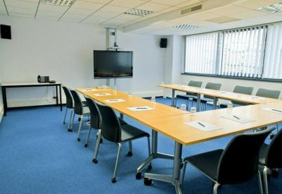 Meeting room with U-shaped table setup, blue floor, and large television screen.