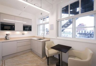 Sleek L-shaped kitchen area with light grey cabinetry and a small dining table.