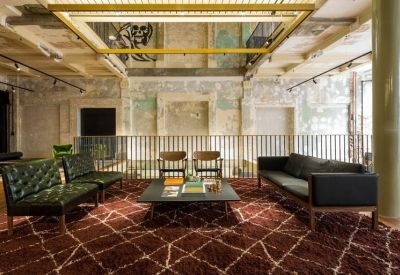 Stylish lounge area with green leather sofas, a patterned rug, and exposed plaster walls.