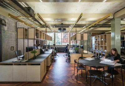 Open-plan workspace with wooden desks, industrial ceilings, and herringbone flooring.