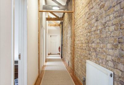Long hallway featuring a characterful exposed brick wall and carpeted floors.