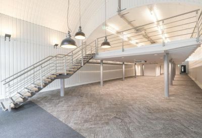 Empty open-plan office space with high ceilings and a steel staircase leading to a mezzanine.