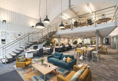 Bright open-plan office with a mezzanine, colourful seating, and a large arched ceiling.