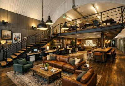 Warm industrial-style lounge area with leather sofas, wood floors, and a neon sign.