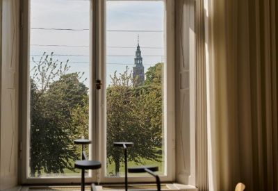 View through a window of a historic church tower and lush green parkland.