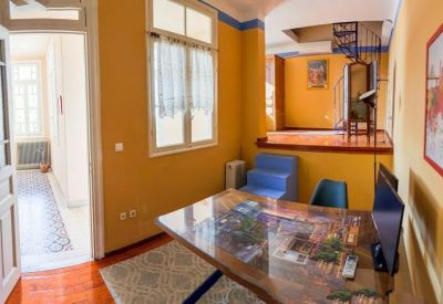 Meeting room featuring a wood-topped table, blue chairs, and a spiral staircase in the background.