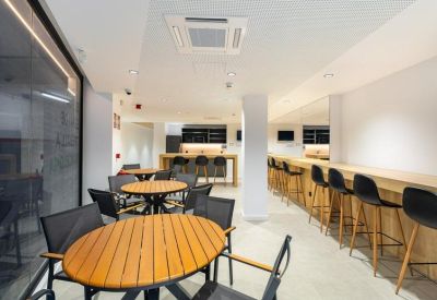 Modern breakout area with round wooden tables, black chairs, and a long wooden bar counter.