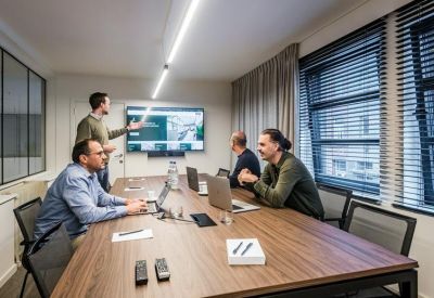 Professional meeting room with a wooden table, large screen, and window blinds.