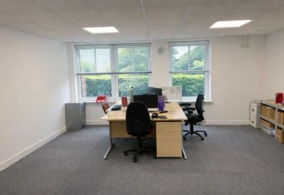 Bright workspace with a four-person desk arrangement and views of green foliage through large windows.