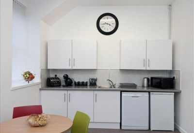 Modern office kitchen with white cabinets, appliances, and a dining table with colourful chairs.