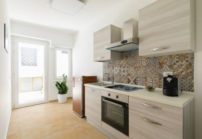 Compact communal kitchen area with light wood cabinets, patterned backsplash, and coffee machine.