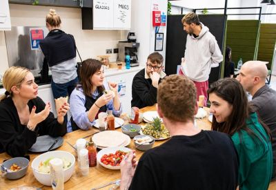 Communal kitchen and dining area with people eating at a long wooden table.