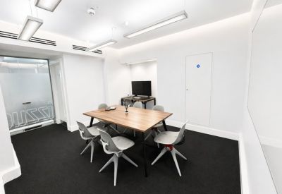 Minimalist meeting room with a wooden table, grey chairs, and white walls.