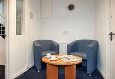 Small waiting area with two blue tub chairs and a round wooden coffee table.