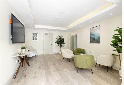 Modern lounge area with pale wood floors, green armchairs, and a large wall-mounted screen.