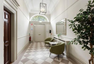 Bright hallway with checkered flooring, olive green armchairs, and a decorative lantern light.