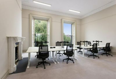 Spacious open-plan workspace with multiple desks, black mesh chairs, and a white fireplace.