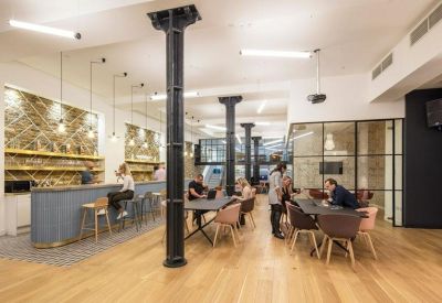 Bright coworking space with a blue bar, long tables, and industrial black pillars.