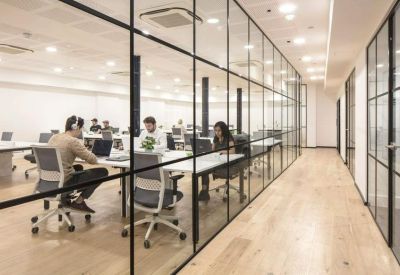 Open-plan office area with rows of white desks behind a glass partition.