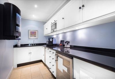 Modern office kitchen with white cabinetry, black countertops, and coffee machines.