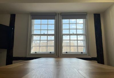 Close-up of a wooden meeting table positioned under classic white-framed sash windows.