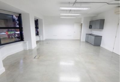 Spacious open-plan office with polished concrete flooring and integrated kitchenette area.