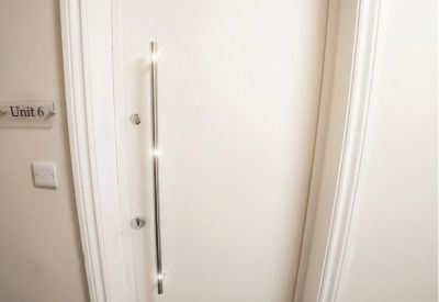 Minimalist white entrance door with a long vertical metal pull handle.