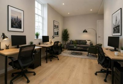 Bright office layout with wood flooring, three workstations, and a grey lounge area in the background.