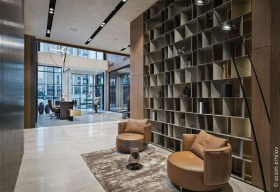 Modern lounge area with comfortable tan armchairs and a floor-to-ceiling bookshelf.